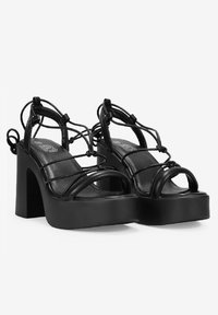 Tacones de plataforma negros con tiras, de diseño minimalista y amplios tacones de bloque. Presentan un acabado en cuero suave y detallados tirantes intrincados.