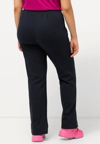 Marineblauwe stretchbroek met een elastische tailleband, licht uitlopende broekspijpen, gecombineerd met roze sportschoenen. Glad textuur, geen patronen.