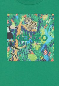 Zelené tričko se živou džunglovou grafikou, na které jsou leopard, tukán, had a různ plants. Potisk obsahuje logo "Kenzo".
