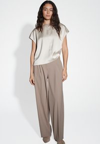 Top beige di seta con maniche a cappuccio e scollo rotondo, abbinato a pantaloni taupe a vita alta con gamba larga.