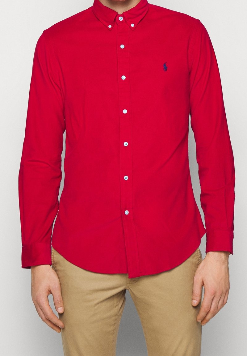 Camicia rossa a bottoni con maniche lunghe, realizzata in cotone. Presenta un colletto a punta e un piccolo logo ricamato sul petto. Design con vestibilità standard.
