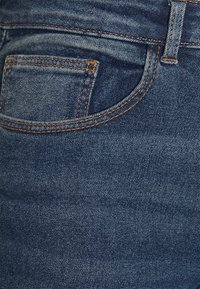 Mörkblå denimjeans med en liten bakficka, kontrasterande orange sömmar och en slät yta. Klassisk design med fem fickor.