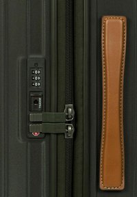 Valigia rigida con un esterno verde scuro testurizzato, doppie cerniere approvate dalla TSA e un manico in pelle marrone.