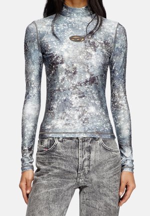 Kvinde iført en tætsiddende, langærmet top med stjernemønster i grå nuancer, kombineret med falmede grå jeans med en subtil glitereffekt.