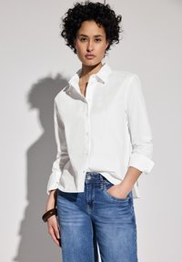 Vit skjorta med krage och uppvikta ärmar, kombinerad med blå jeans. Slät tyg med en avslappnad passform och subtil lyster.
