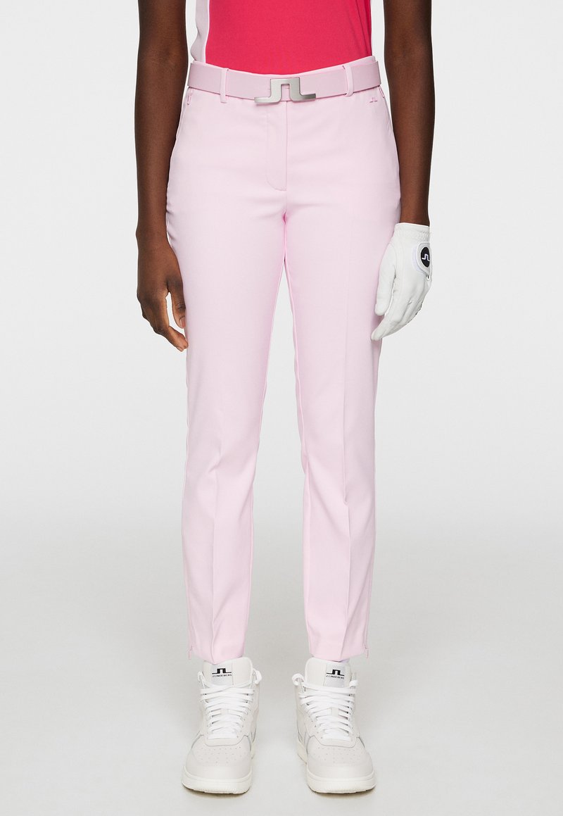 Rosa skräddarsydda golfbyxor med slim fit, utrustade med en silvermetallspänne. Bärs med en vit golfhandske och vita sneakers.