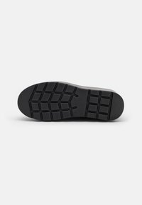Suela de goma negra con profundos surcos geométricos y secciones de puntera y talón texturizadas, diseñadas para ofrecer agarre y durabilidad.