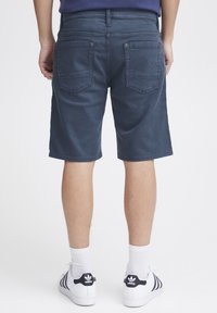 Navy modri šorts iz bombažne mešanice, s ravnim krojem, dvema zadnjima žepoma in ravnim pasom. Nosi se z belimi supergami.