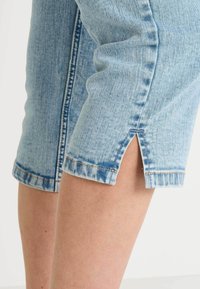 Pantalones cortos de mezclilla azul claro con dobladillo deshilachado, que cuentan con aberturas laterales y costuras en contraste. La tela muestra un ligero desgaste y un patrón desvanecido.