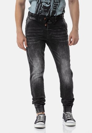 Black denim jogger pants with a slightly faded finish, elastic waistband, adjustable drawstring, and ribbed cuffs. Paired with black sneakers.