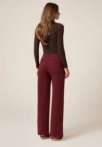 Bordeaux-brede wijde broek met een hoge taille, voorzien van twee achterzakken en metalen accenten, gecombineerd met een strakke bruine longsleeve top.