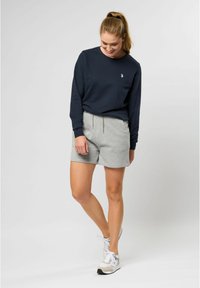 Marinblå långärmad sweatshirt med liten logotyp, matchad med ljusgrå shorts med elastisk midja och snörning. Avslappnade sportskor.