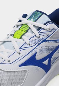 Λευκό και μπλε αθλητικό παπούτσι με λευκά κορδόνια, μπλε λογότυπο στο πλάι και φωσφοριζέ πράσινη λεπτομέρεια στη γλώσσα.