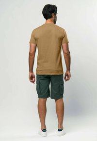 Khaki krāsas īsām piedurknēm T-krekls, kokvilnas maisījums, noapaļota apkakle; pārī ar zaļiem cargo šortiem ar sānu kabatām, valkāti ar baltām sporta apaviem.