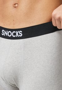 Boxer di colore grigio con una fascia nera che presenta la scritta bianca "SNOCKS". Il tessuto sembra morbido e ha una superficie liscia.