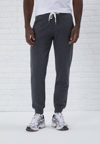 Graue Jogginghose mit einem Zugbandbund und gerippten Bündchen, kombiniert mit silbernen und schwarzen Sportschuhen. Merkmale einen glatten Stoffeinsatz.