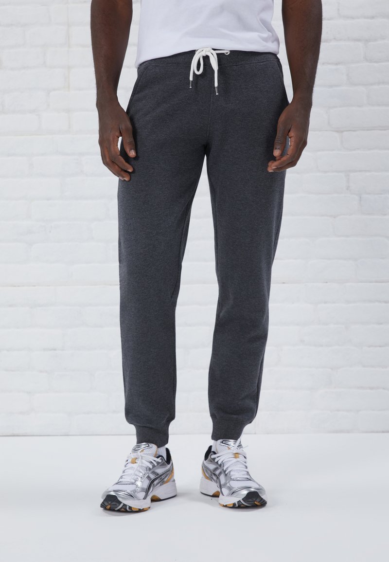 Graue Jogginghose mit einem Zugbandbund und gerippten Bündchen, kombiniert mit silbernen und schwarzen Sportschuhen. Merkmale einen glatten Stoffeinsatz.