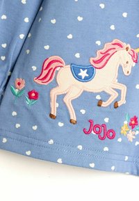 Plava majica s uzorkom bijelih srca, izvezena jednorogom s ružičastom grivom, plavim sedlom i ružičastim cvjetnim detaljima. Ime "Jojo" je izvezeno u ružičastoj boji.