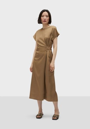 Robe en satin marron avec des manches courtes, dotée d'un devant en wrap et d'un détail de taille nouée. Texture lisse, longueur mi-mollet, associée à des sandales à brides.