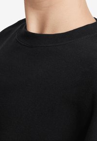 Svart crewneck sweatshirt med en ribbad halsringning och mjukt tyg. Kragen och axlarna är smidigt sydda.