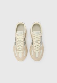 Beežid seemisnahast tossud kreemikate detailidega, paelaga kinnitatavad, tekstuurse tallaga ja küljes peegeldava hõbedase logoga.