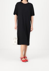 Musta lyhythihainen mekko rennolla istuvuudella, yhdistettynä pieneen valkoiseen käsilaukkuun ja punaisiin korkokenkiin, joissa on terävät varpaat.