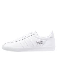 Vita Adidas Gazelle-sneakers med slät läder, tre sidostreck, en texturerad gummisula och en logolapp på utsidan.