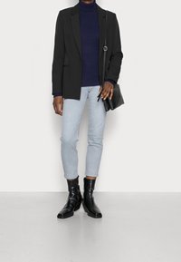 Blazer noir sur un col roulé côtelé bleu marine, jean bleu clair et bottines noires. Comprend un petit sac bandoulière noir.