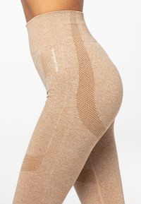 Bēša augstās jostas bikses ar tekstūru un sietu izstrādājumam sānos. Satur logotipu, kas drukāts uz gurniem. Mīksts, elastīgs audums.