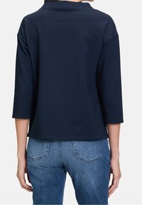 Sudadera navy corta con mangas tres cuartos, textura suave y escote ancho, combinada con jeans de mezclilla azul claro con bolsillos traseros.