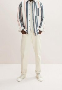 Koszula w paski w kolorze niebieskim, różowym i białym, zestawiona z kremowymi spodniami i białymi sneakersami. Posiada kieszeń na piersi.