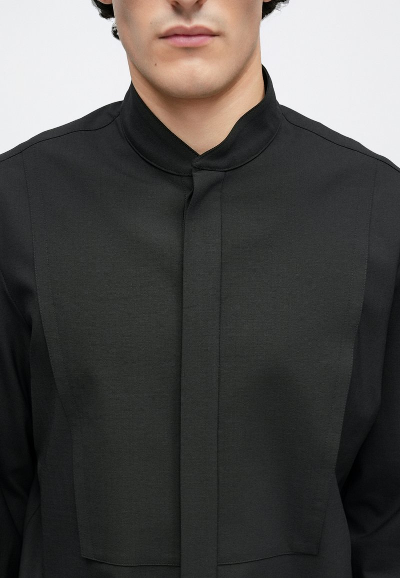 Schwarzes Hemd zum Knöpfen mit hohem Kragen, strukturiertem Stoff und einem zentralen Panel-Design. Minimalistischer und eleganter Schnitt.