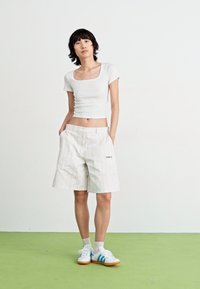 Top cropped branco ajustado com mangas curtas, combinado com calções brancos de riscas até ao joelho, usados com ténis brancos e azuis.