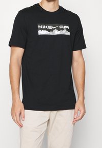 Black cotton t-shirt featuring a rectangular white Nike Air logo with a cloud graphic. Short sleeves and a crew neckline.