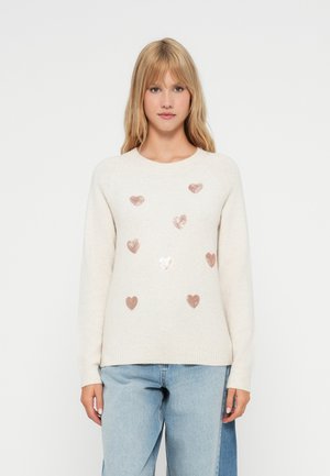 Cream sweater with a round neckline and long sleeves, adorned with metallic rose gold heart patterns, paired with light blue jeans.