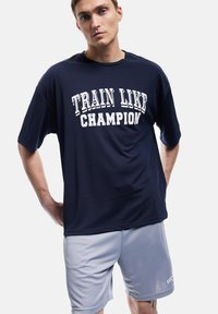 Marineblå atletisk T-shirt med hvid tekst "TRAIN LIKE CHAMPION", sammen med lysegrå shorts lavet af blødt, åndbart stof.