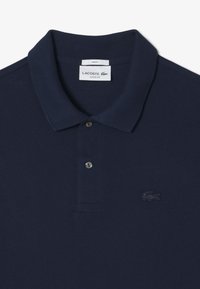 Navyblå bomullspolo med en strukturerad yta, placket med två knappar och Lacoste-logotypen broderad i matchande färg på bröstet.