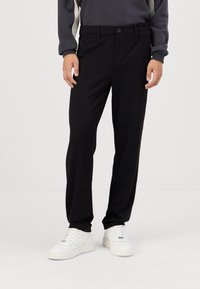 Czarne spodnie wykonane z gładkiego materiału, o slim fit, z paskami na pasek i pojedynczym zapięciem na guzik. W zestawie z białymi sneakerami.