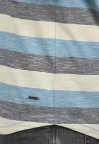 Gestreepte stof in lichtblauw, donkerblauw, grijs en crème kleuren. Bevat metalen label "ISOLID" met contrasterende stiksels.