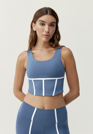 Modrý športový crop top s bielymi akcentmi, má priliehavý strih a široké ramienka. Hladká textúra, určený na aktívne nosenie.