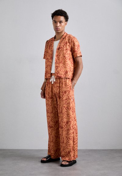 L'ensemble comprend une chemise à manches courtes ornée d'un motif floral orange et un pantalon ample assorti, avec une taille à cordon et une coupe décontractée.