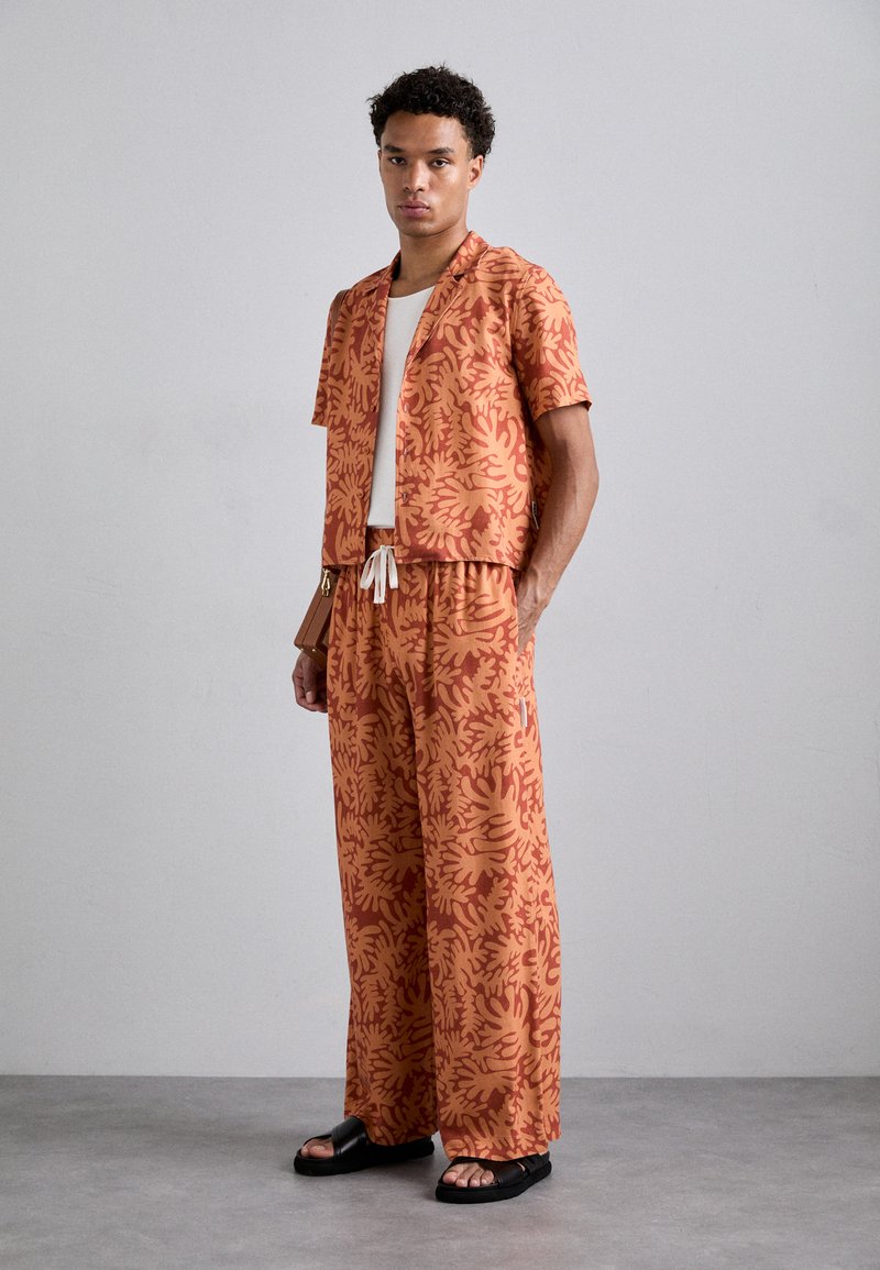 Set includes an orange floral-patterned short-sleeve shirt and matching wide-leg pants, featuring a drawstring waist and a relaxed fit.