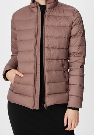 Vrouw met een stofroze doorgestikte jas met ritssluiting aan de voorkant en zijzakken, gecombineerd met een zwarte top en rok.