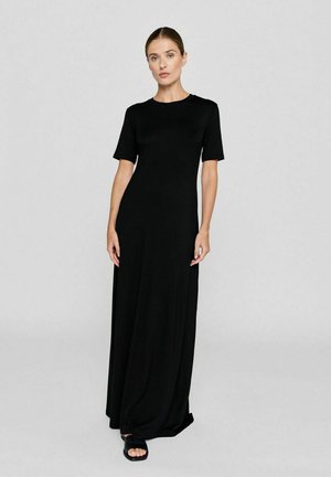 Zwarte maxi-jurk met korte mouwen van lichte stof, met een ronde halslijn en een vloeiende silhouet. G gedragen met platte, open teen sandalen.