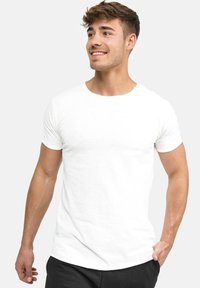 White cotton t-shirt with short sleeves, round neckline, and a relaxed fit. Smooth texture with minimal detailing. Worn with black pants.