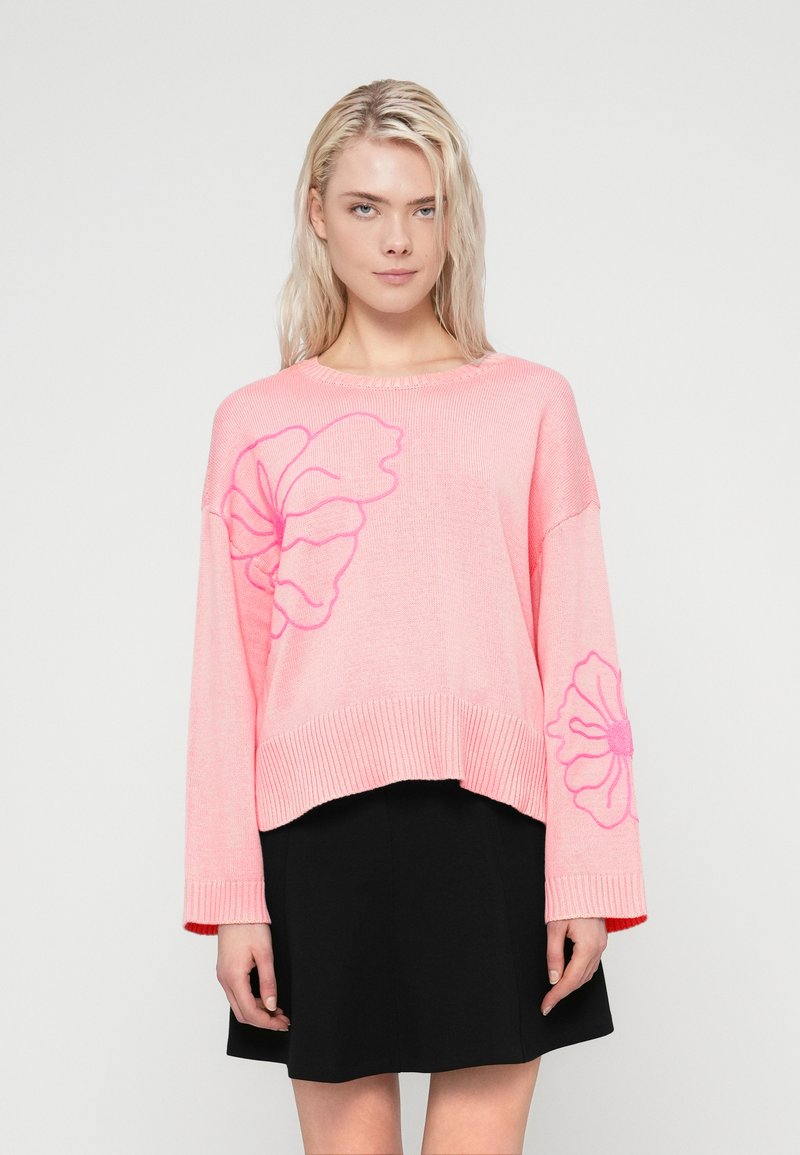 Ροζ υπερμεγέθη πουλόβερ με μακριά μανίκια, διακοσμημένο με ροζ ανθισμένα σχέδια. Ριμπ καβάλο και τελείωμα, σε συνδυασμό με μαύρη φούστα. Μαλακή υφή.