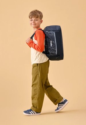 Backpack with a dark blue exterior featuring a lightning pattern, carried by a child wearing a beige and orange long-sleeve shirt and olive pants.