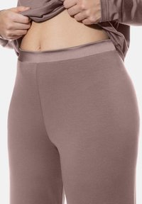Taupe leggings met een gladde textuur en een elastische tailleband, gedeeltelijk zichtbaar onder een losse top, die een aansluitend ontwerp toont.