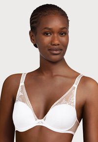 Reggiseno bianco in pizzo con pannelli trasparenti, coppe lisce e dettagli decorativi lungo i bordi. Spalline regolabili per migliorare la vestibilità e il comfort.