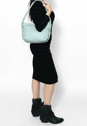 Donna con vestito nero che indossa stivaletti neri con frange alla caviglia e tiene una borsa a tracolla azzurro chiaro con tracolla intrecciata.